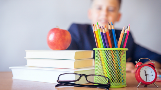 Pencils in a cup on a desk with glasses, book, and apple and a student