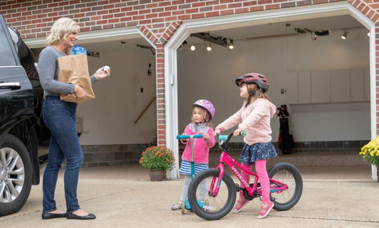 Mother holding a garage door opener remote with children outside on a bike and scooter