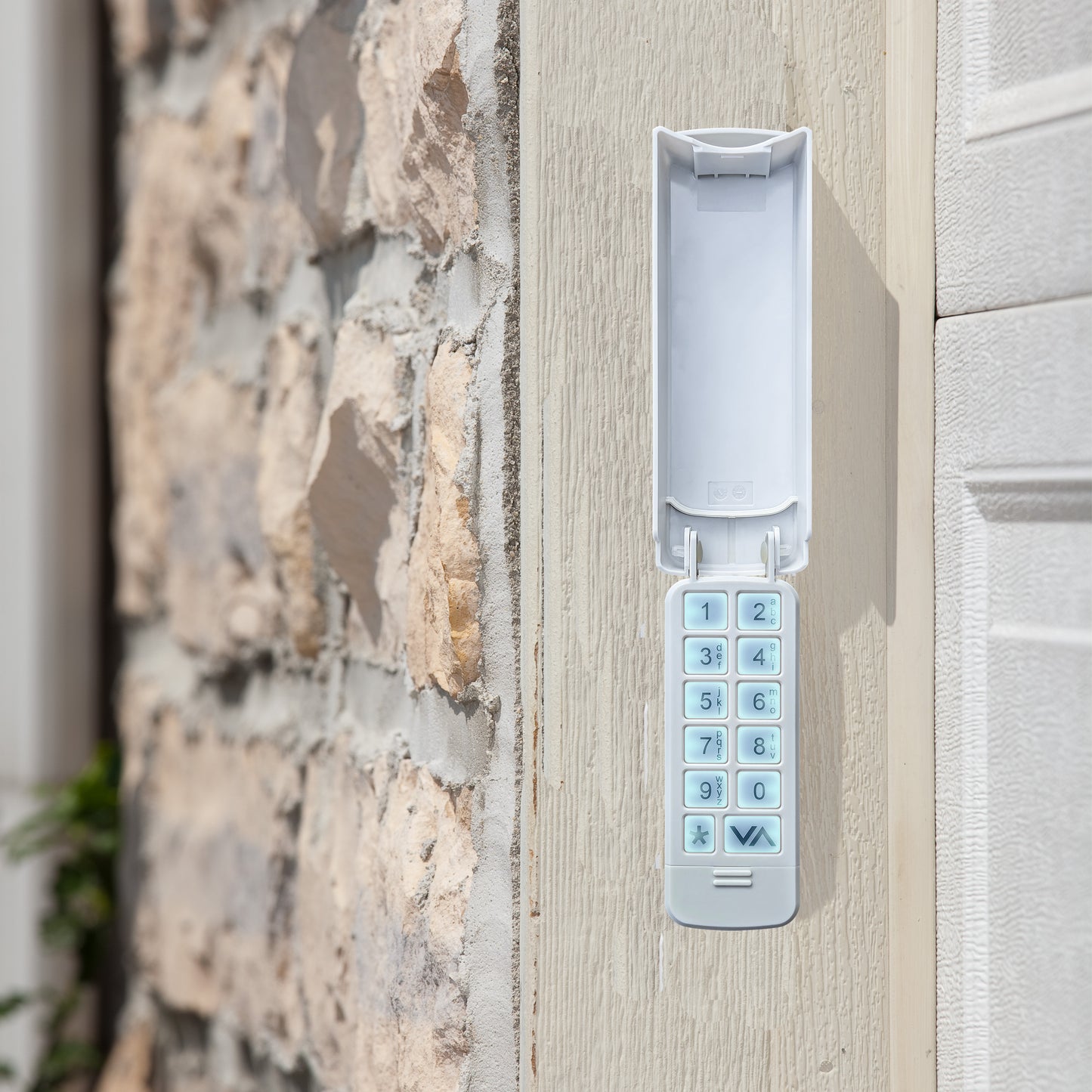 A white electronic keypad lock mounted on a light-colored wooden door next to a stone wall.