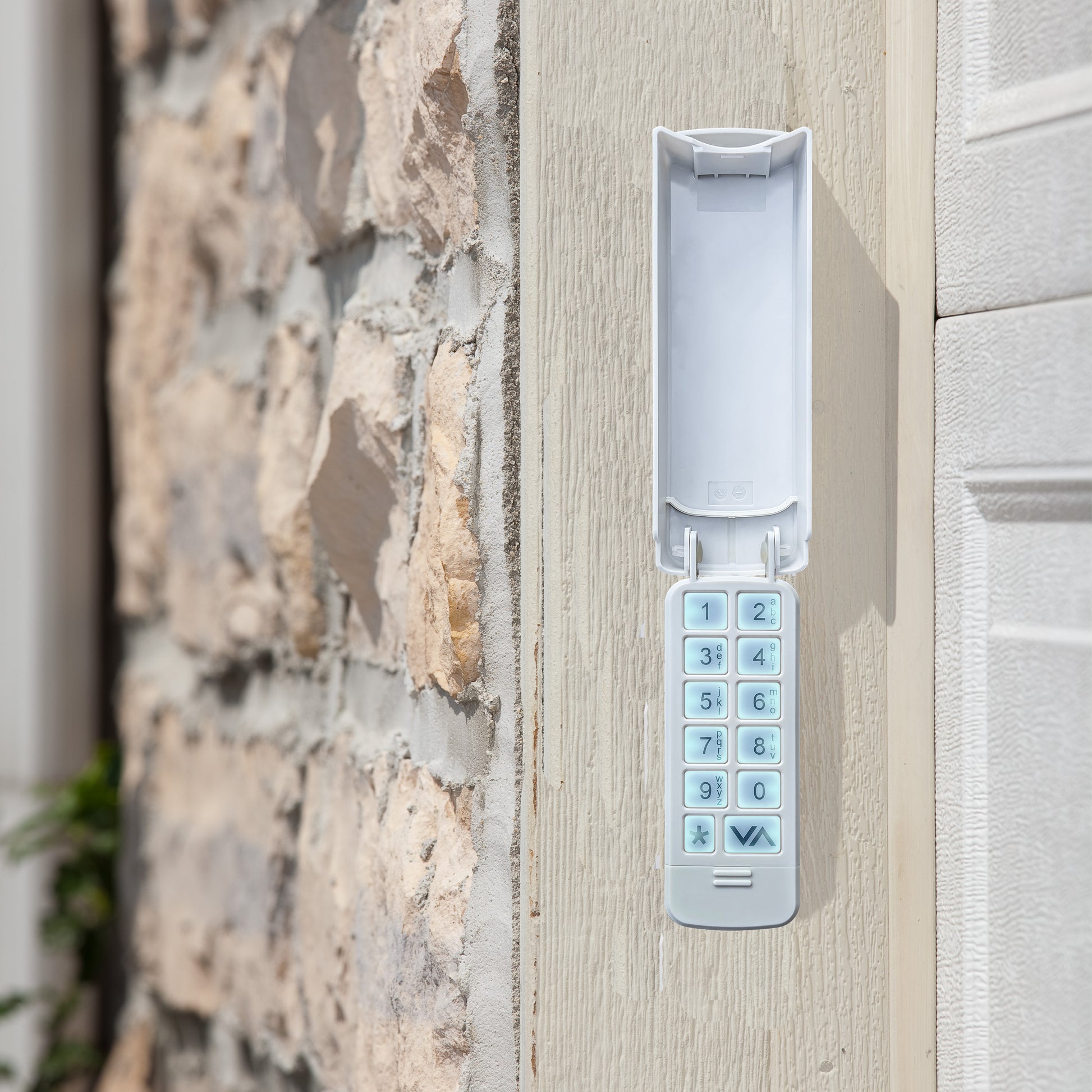 A white electronic keypad lock mounted on a light-colored wooden door next to a stone wall.